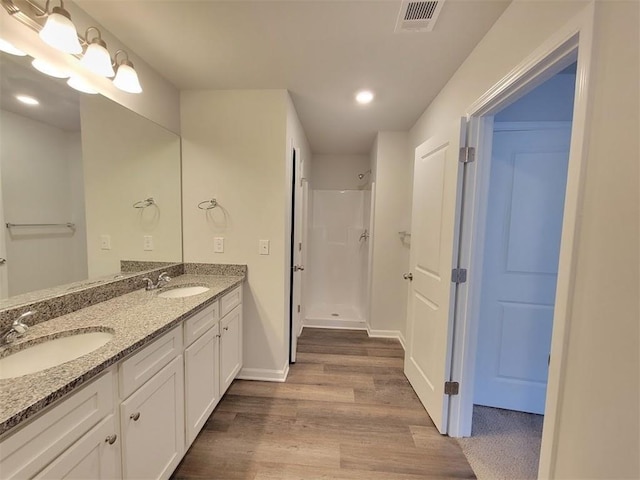 full bathroom with wood finished floors, a stall shower, double vanity, baseboards, and recessed lighting
