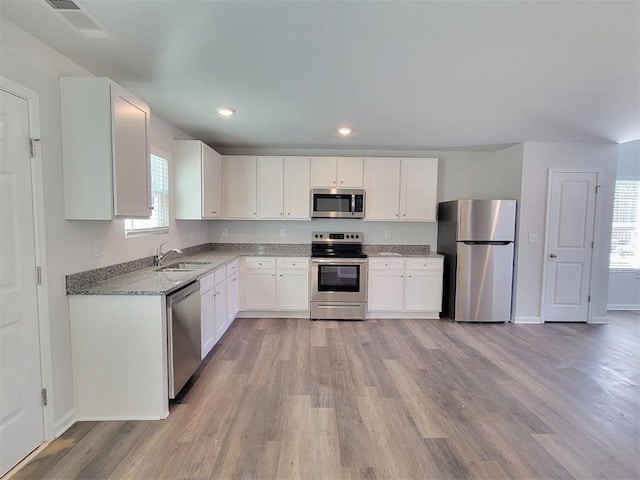kitchen featuring appliances with stainless steel finishes, a sink, light wood-type flooring, baseboards, and white cabinetry