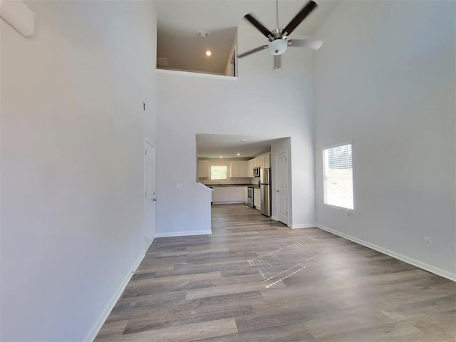 unfurnished living room with a towering ceiling, a ceiling fan, light wood-type flooring, baseboards, and recessed lighting
