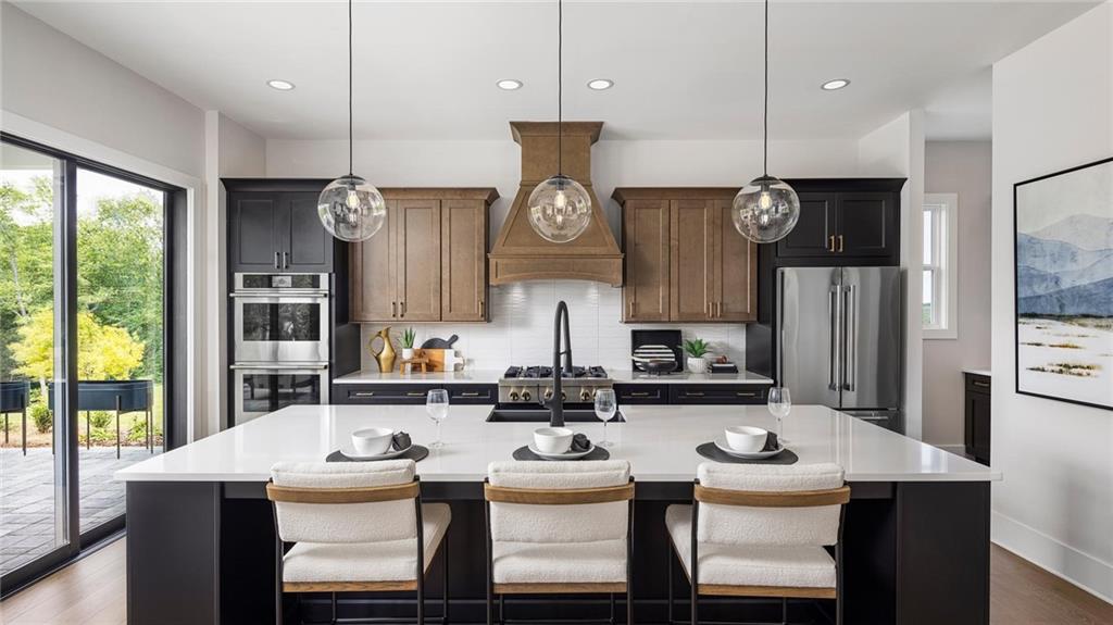 kitchen with hardwood / wood-style floors, pendant lighting, a kitchen island with sink, and stainless steel appliances