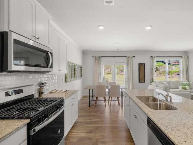 kitchen with appliances with stainless steel finishes, light stone counters, ornamental molding, white cabinets, and decorative backsplash