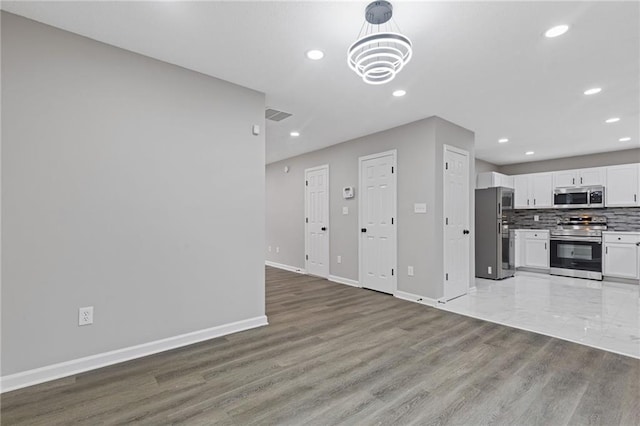 kitchen featuring appliances with stainless steel finishes, white cabinetry, backsplash, wood-type flooring, and a chandelier