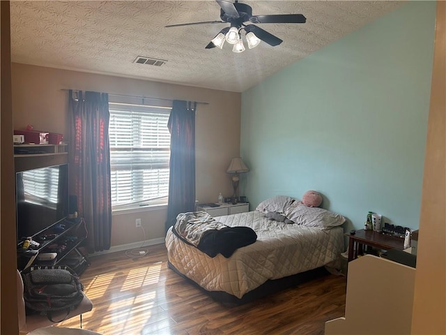 bedroom with a ceiling fan, a textured ceiling, visible vents, and wood finished floors