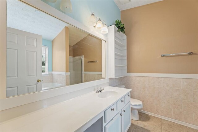 bathroom featuring a textured ceiling, toilet, vanity, tile walls, and tile patterned floors