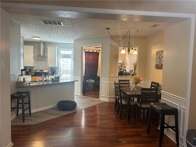 dining room with a wainscoted wall, wood finished floors, visible vents, and an inviting chandelier