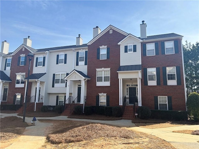 multi unit property featuring a standing seam roof, brick siding, metal roof, and a chimney