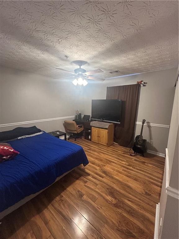 bedroom with ceiling fan, a textured ceiling, baseboards, and wood finished floors