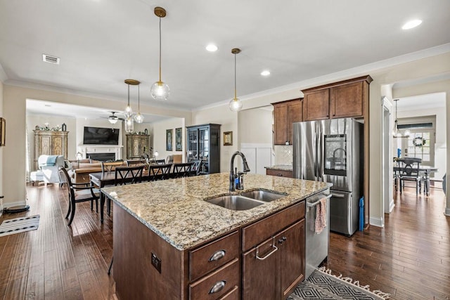 kitchen with appliances with stainless steel finishes, sink, ornamental molding, light stone counters, and a center island with sink