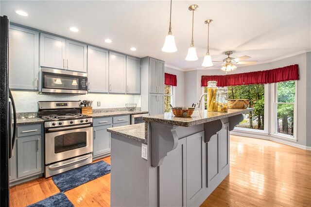 kitchen featuring light wood finished floors, gray cabinets, ornamental molding, and appliances with stainless steel finishes