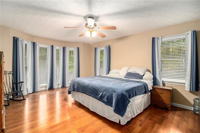 bedroom featuring baseboards, multiple windows, wood finished floors, and a ceiling fan