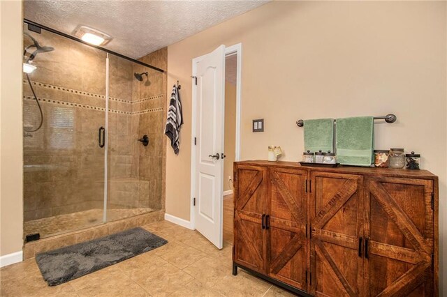 bathroom featuring tile patterned floors, a textured ceiling, baseboards, and a stall shower