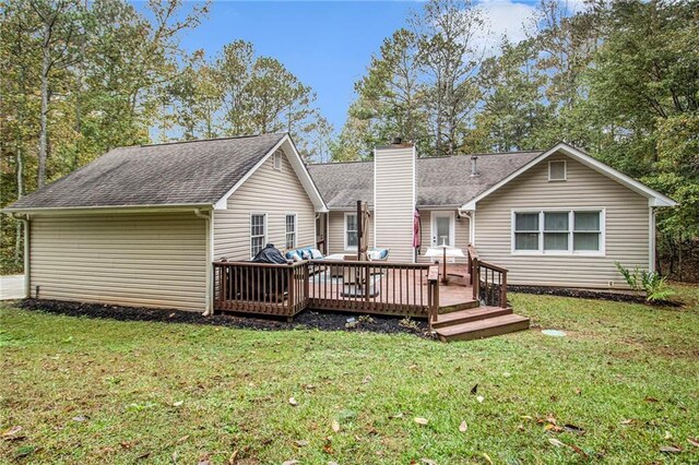 back of property with roof with shingles, a deck, a chimney, and a lawn