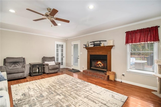 living room featuring a glass covered fireplace, wood finished floors, ornamental molding, and ceiling fan