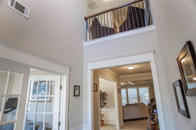 corridor with a wainscoted wall, visible vents, crown molding, and a high ceiling