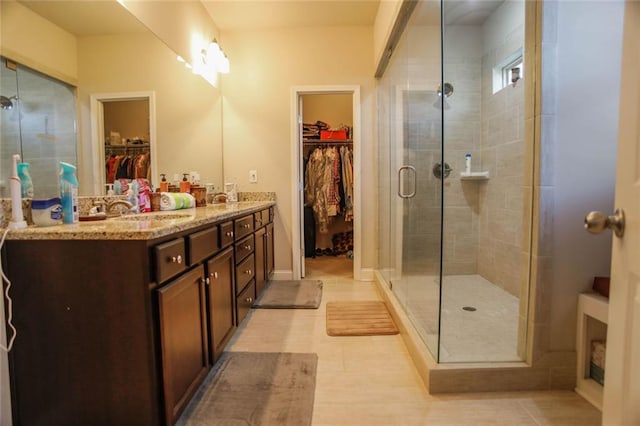 bathroom featuring tile patterned flooring, a sink, a shower stall, double vanity, and a walk in closet