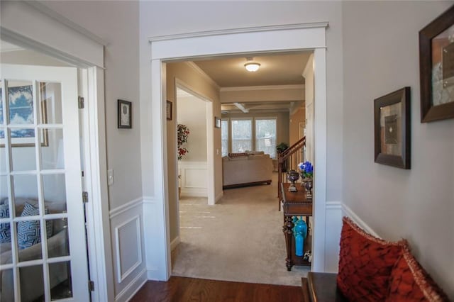 hallway with a wainscoted wall, ornamental molding, stairs, dark carpet, and a decorative wall