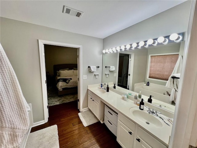 bathroom featuring visible vents, a garden tub, a sink, wood finished floors, and double vanity