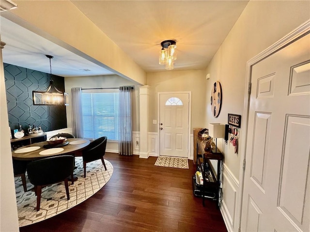 foyer entrance with a chandelier, dark wood finished floors, and wainscoting