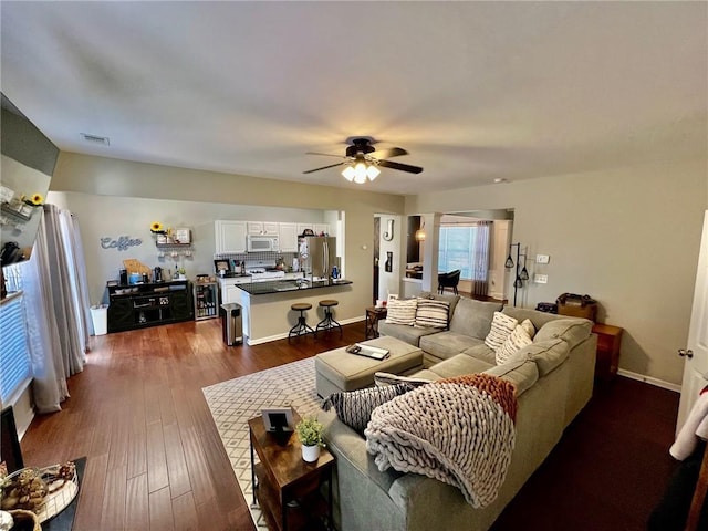 living room featuring visible vents, baseboards, a ceiling fan, and dark wood-style flooring