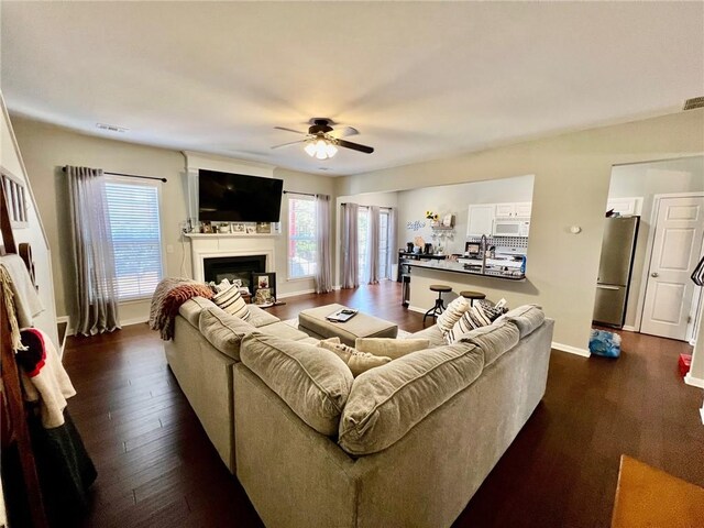 living room with dark wood-type flooring, plenty of natural light, a fireplace, and ceiling fan