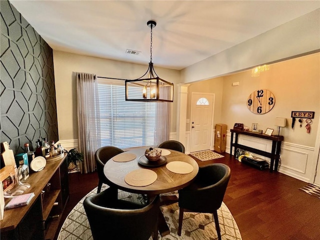 dining room featuring dark wood finished floors, visible vents, a decorative wall, and a wainscoted wall