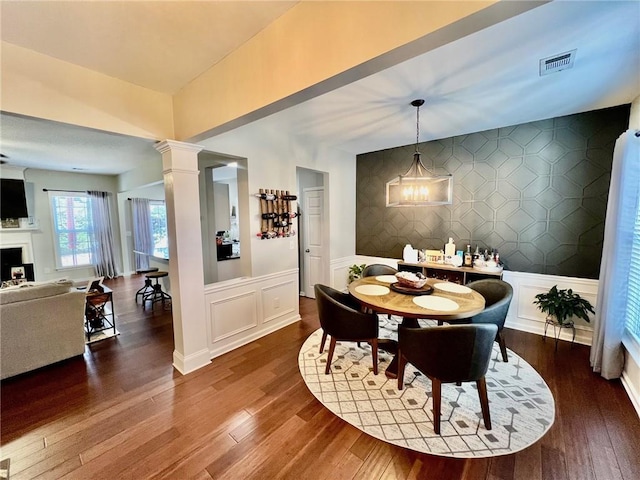 dining area with visible vents, an accent wall, a decorative wall, decorative columns, and dark wood-style flooring