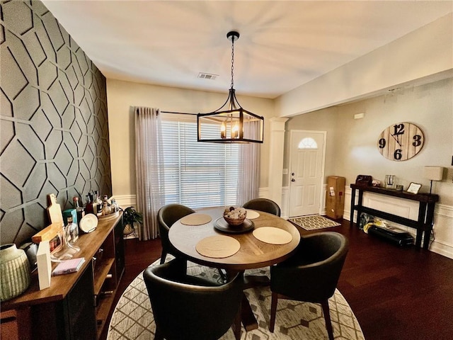 dining area with visible vents, dark wood-type flooring, decorative columns, a chandelier, and an accent wall