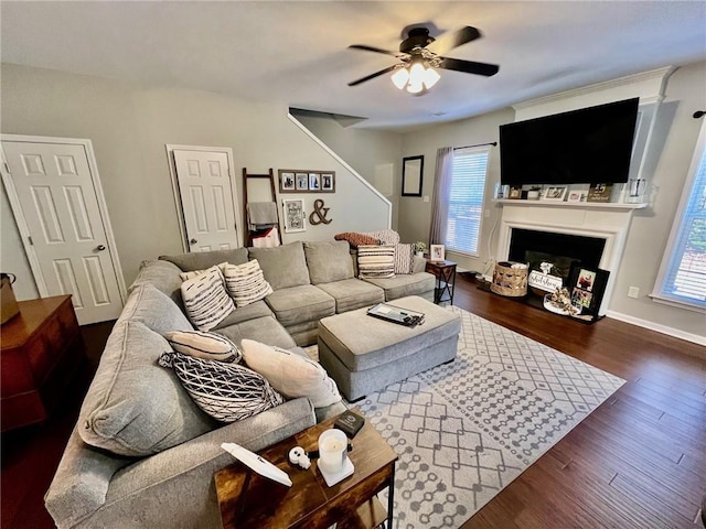 living area featuring a fireplace, dark wood-style floors, baseboards, and ceiling fan