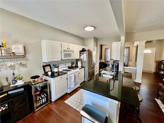 kitchen with a kitchen breakfast bar, white cabinets, white appliances, ornate columns, and a sink