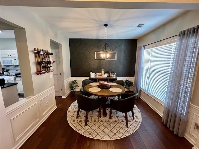 dining space featuring an accent wall, dark wood-style floors, visible vents, and wallpapered walls