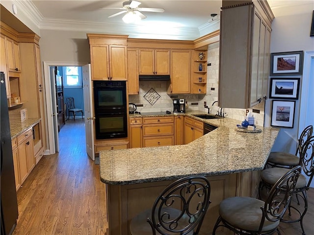 kitchen with sink, light stone counters, a kitchen breakfast bar, black appliances, and kitchen peninsula