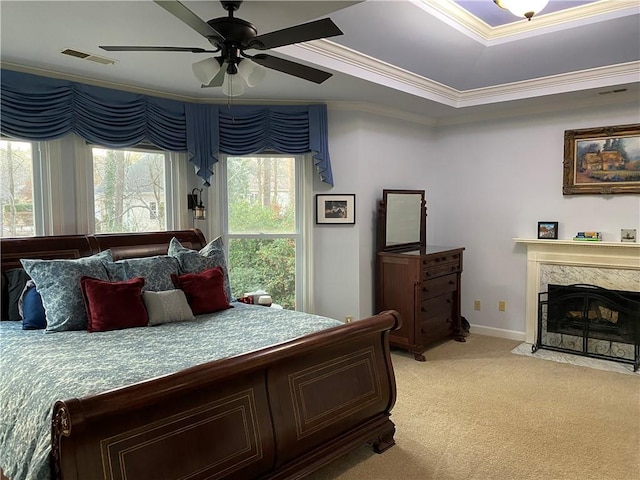 bedroom featuring a high end fireplace, a tray ceiling, ornamental molding, ceiling fan, and light carpet