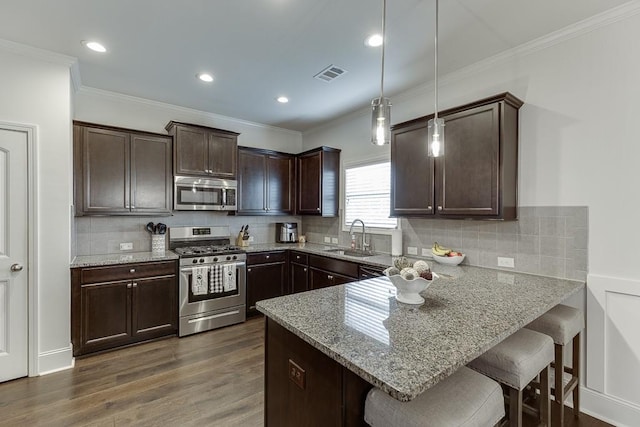 kitchen with kitchen peninsula, hanging light fixtures, appliances with stainless steel finishes, sink, and a kitchen bar