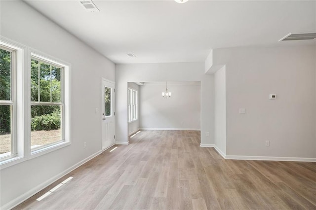 unfurnished room with a chandelier, light wood-style floors, and baseboards