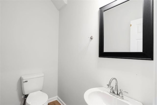 half bathroom with a sink, toilet, and baseboards