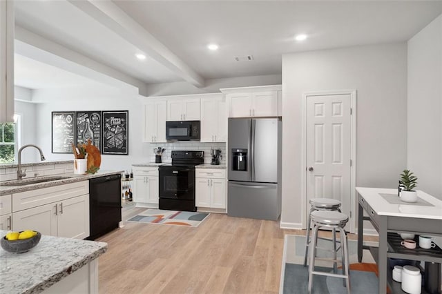 kitchen featuring black appliances, a sink, white cabinetry, decorative backsplash, and light wood-style floors