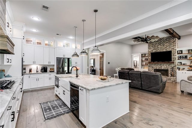 kitchen featuring white cabinetry, hanging light fixtures, a center island with sink, light stone countertops, and black fridge