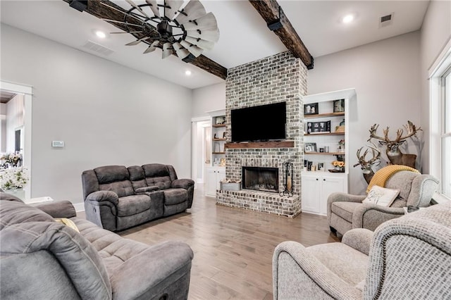 living room featuring ceiling fan, a brick fireplace, beamed ceiling, and light wood-type flooring