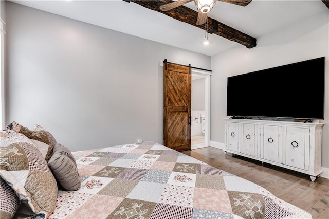 bedroom featuring beamed ceiling, wood-type flooring, a barn door, and ceiling fan