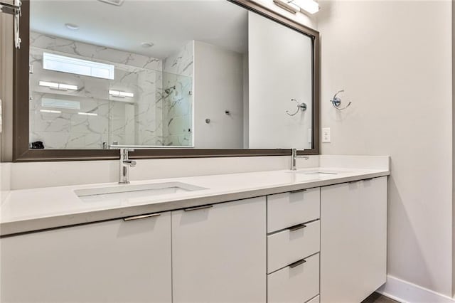 bathroom with a marble finish shower, double vanity, baseboards, and a sink