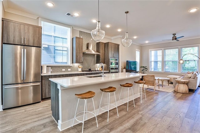 kitchen featuring wall chimney range hood, visible vents, stainless steel appliances, a kitchen breakfast bar, and open floor plan