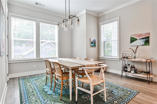 dining space with baseboards, wood finished floors, visible vents, and ornamental molding