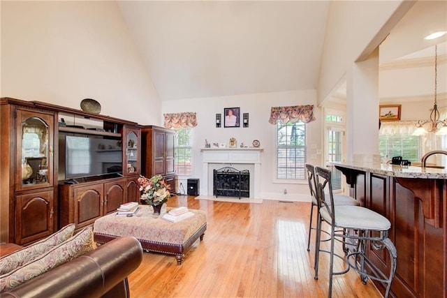 living room featuring light wood-type flooring, high vaulted ceiling, a chandelier, and sink