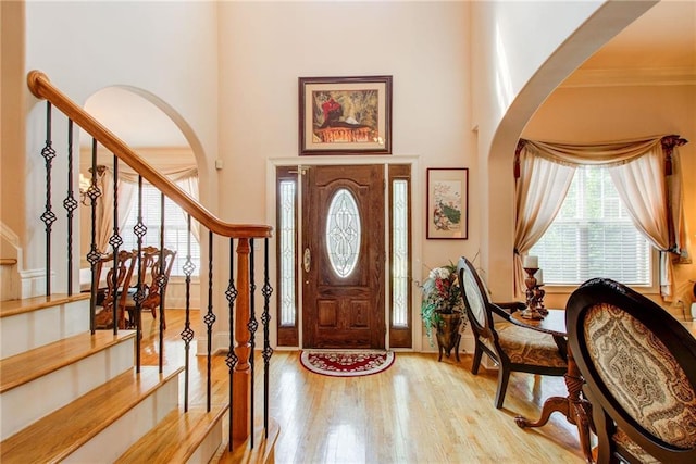 foyer featuring light wood-type flooring, crown molding, and a towering ceiling