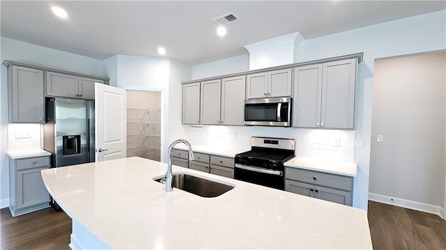 kitchen featuring an island with sink, sink, gray cabinetry, dark wood-type flooring, and appliances with stainless steel finishes