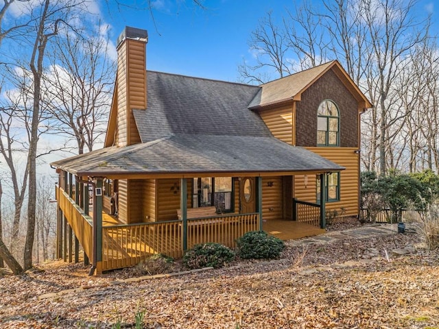 chalet / cabin with log veneer siding, a porch, a chimney, and roof with shingles