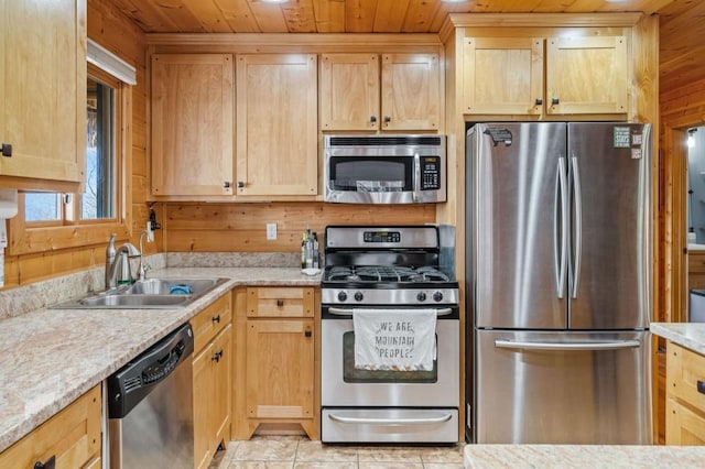 kitchen with wooden walls, light brown cabinets, wooden ceiling, stainless steel appliances, and a sink