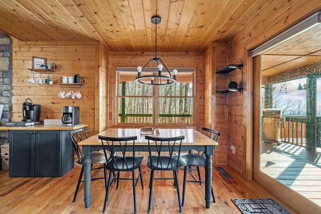 dining room featuring an inviting chandelier, wood ceiling, wood walls, and light wood finished floors