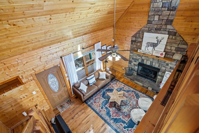 unfurnished living room featuring high vaulted ceiling, a ceiling fan, wood finished floors, wood walls, and a fireplace