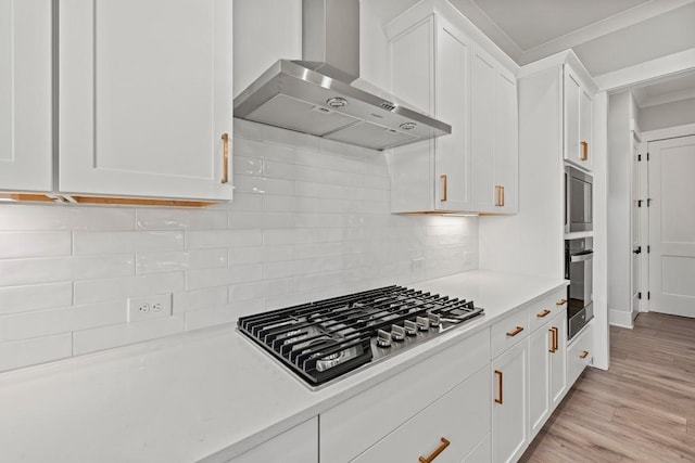 kitchen featuring white cabinets, light countertops, wall chimney range hood, appliances with stainless steel finishes, and decorative backsplash